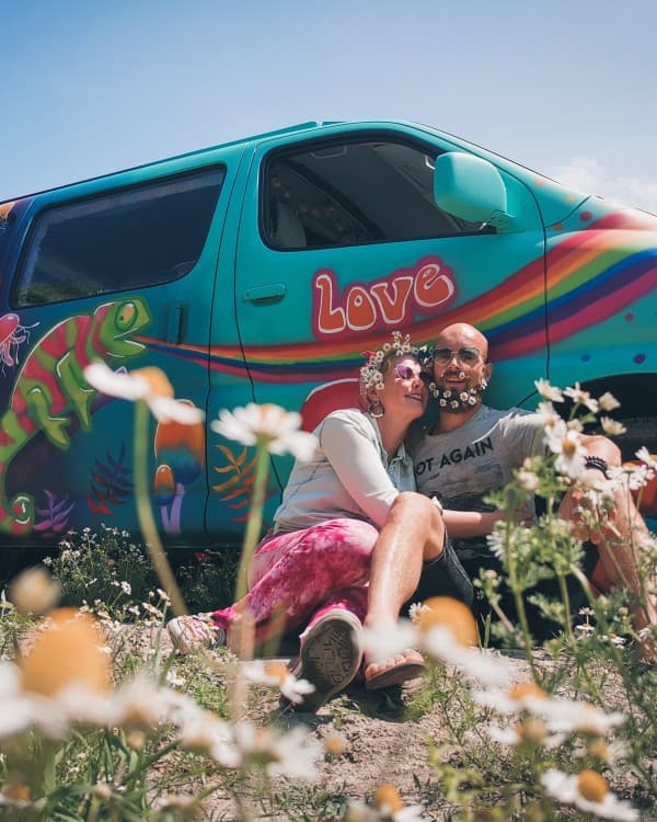 Joriën and Sandra and their hippie van - @travelwildtobefree 08/2021 Joriën and Sandra from travelwildtobefree, sitting amidst wildflowers, smiling and enjoying nature in front of their colorful, hippie-themed Toyota HiAce 4x4 camper van.