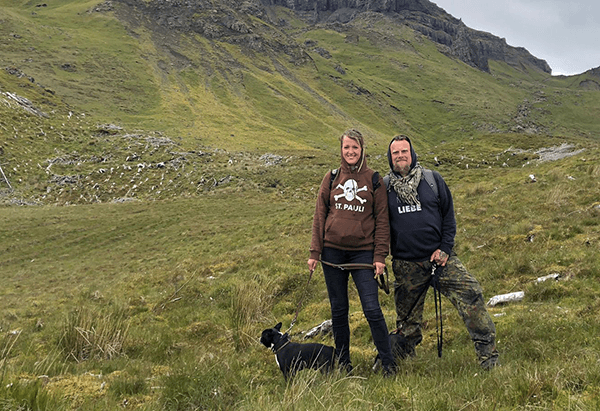 Discovering the highlands of Scotland - @leinen_los_zu_viert_ 06/2024 A couple, Andre and Marina from @leinen_los_zu_viert_, stand in a scenic, grassy area in Scotland, smiling with their two dogs, Pupe and Erna. They are dressed in casual outdoor clothing, enjoying a peaceful hike in the lush, mountainous landscape. This image captures their adventurous spirit and love for nature during their van life journey.