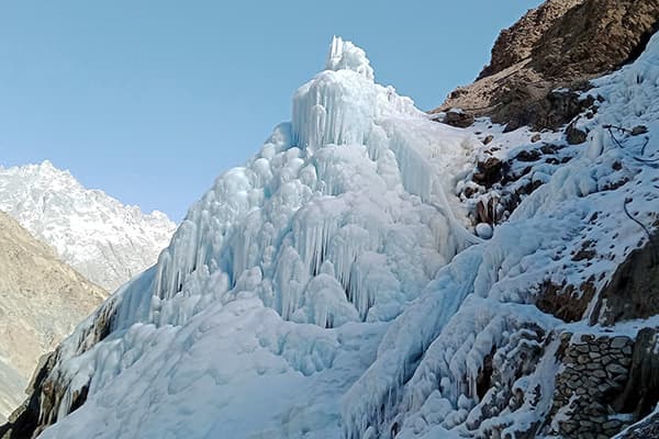 Tall ice cones hold the water and melt slowly in summer - @advandortmontduurzaam 04/2025 Large manmade ice tower built on a steep mountain slope in the Karakoram region of northern Pakistan, designed to store winter meltwater as frozen ice for use during the dry summer months. The towering cone-shaped ice structure features intricate layers of frozen cascades and icicles, with water visibly frozen into thick, sculptural forms. Rocky terrain and snow-covered peaks surround the ice tower under a clear blue sky. These sustainable ice towers are part of local climate adaptation strategies, helping to irrigate crops and reduce flood risks in high-altitude glacier regions.