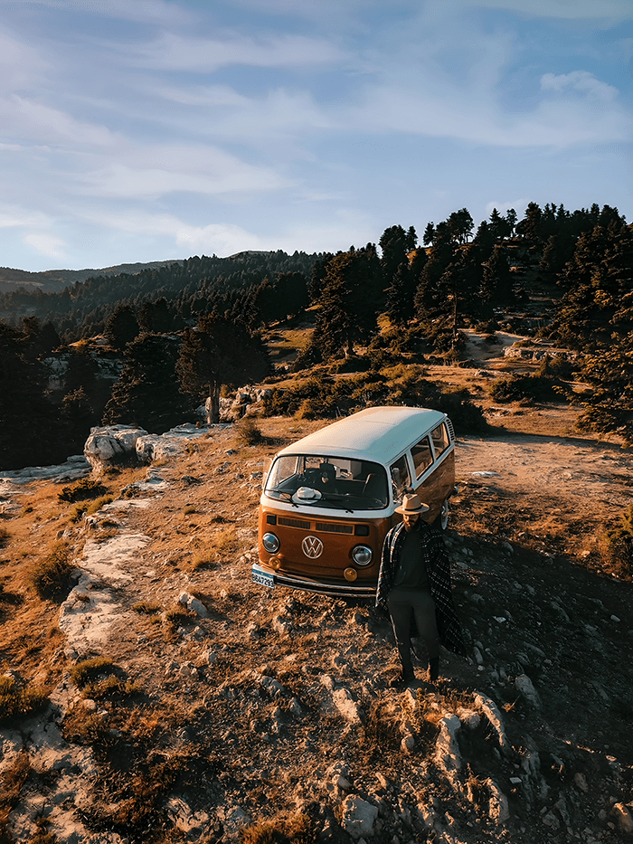 I discovered an innate love for nature - @gero0oooo 12/2022 Gregory Kamel, also known as @gero0oooo, standing beside a restored vintage Volkswagen T2 camper van parked on a rocky mountain plateau in Lebanon, surrounded by pine trees and golden hour sunlight. The scenic landscape highlights the rugged beauty of Lebanese nature and the spirit of solo vanlife travel, off-grid camping, and adventure.