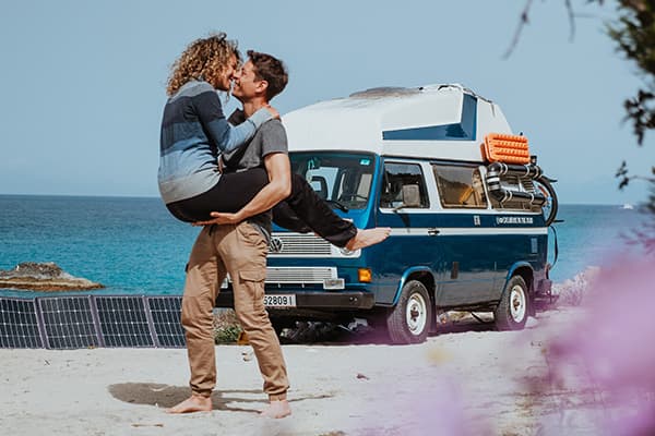 The Best Thing That Could Have Happened to Us - @edelweiss.on.the.road 06/2022 Thomas & Regina, from @edelweiss.on.the.road, are pictured on a beautiful beach in Lefkada, Greece. In this intimate moment, Thomas lifts Regina as they share a kiss, with their VW T3 Vanagon "Edelweiss" parked in the background near the turquoise waters. Solar panels are set up beside the van, highlighting their off-grid vanlife setup. The serene ocean and clear blue sky create a perfect backdrop, reflecting the freedom and romance of their vanlife adventure along the idyllic Greek coastline.