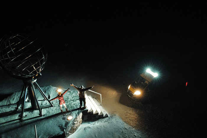 A highlight for us: the North Cape in Norway - @gary_and_sheila 06/2023 Nighttime scene at the North Cape in Norway showing Gary and Sheila standing with raised arms beside the iconic globe monument, illuminated by lights and surrounded by snow and darkness. Their yellow self converted Fiat Ducato camper van is parked nearby with headlights on, capturing winter vanlife, Arctic travel, extreme conditions, and the long distance overland journey of @gary_and_sheila to the northernmost drivable point of mainland Europe.