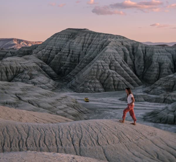 A gift of vanlife: connecting with nature - @our_orbit_vanlife 07/2024 A woman, Astrid from @our_orbit_vanlife, in casual clothing walks on a rugged, rocky terrain at sunset in Nallıhan Ankara, Turkey. In the background, a yellow Mercedes Vario 816D camper van is parked among dramatic, eroded rock formations, highlighting the adventurous spirit and natural beauty of vanlife.