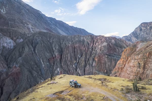 The beauty of South America's nature - @_roadtales 11/2024 A Puch 230GE 4x4 offroad camper parked on a grassy plateau overlooking dramatic, multicolored cliffs and rugged mountains in the Cotahuasi Canyon in Peru.