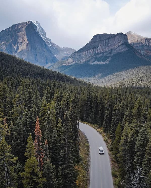 "It’s the unknown that ultimately fuels me to move forward" - @christiandelatorre_ 09/2022 Christian de la Torre's (@christiandelatorre_) white 1984 VW T3 Westfalia camper van drives along a winding road through dense evergreen forests, surrounded by the towering Rocky Mountains in Banff National Park, Alberta, Canada. The breathtaking landscape, with its snow-capped peaks and serene wilderness, embodies the adventurous van life lifestyle. This moment captures Christian’s journey of exploring remote and awe-inspiring destinations, as described in his article about living on the road and embracing freedom and discovery.