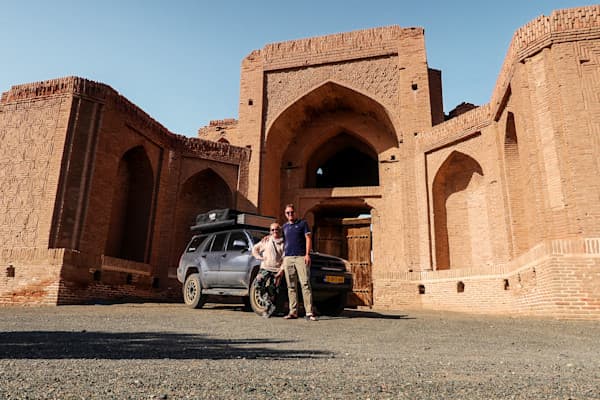 Charelle & Marcel at a Silk Road Caravansarai in Iran - @char.is.far 01/2025 Charelle and Marcel from @char.is.far standing in front of their Toyota 4Runner with a rooftop tent at a historic Silk Road caravanserai in Iran. The background features intricate brickwork and an arched gateway, showcasing Persian architectural heritage. The image highlights their overlanding adventure through Iran, part of a larger journey from Europe to Asia.