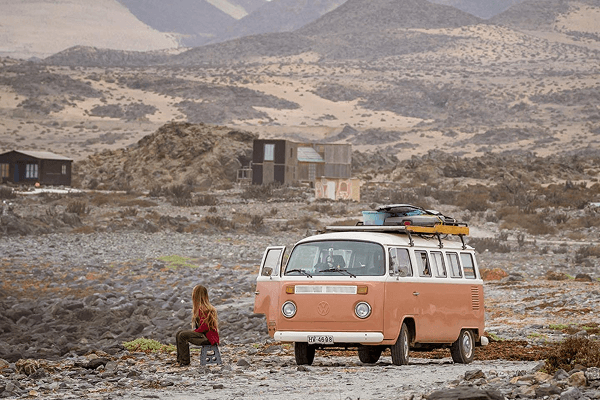Visiting different destinations in the country - @octaviaviajando 09/2022 Victoria from Chile, creator of @octaviaviajando, sits on a small stool next to her pink and white 1985 Volkswagen Kombi parked on a rocky desert landscape in northern Chile. Surrounded by arid hills and sparse structures, the scene reflects the solitude and serenity of off-grid vanlife. Captured during her solo journey, this moment highlights her commitment to slow travel, self-sufficiency, and connecting deeply with remote places and natural environments.