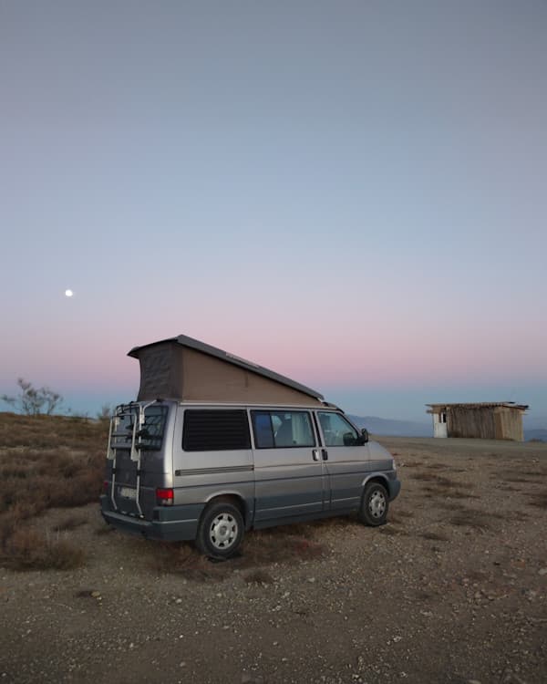 My VW T4 in twilight near Canjáyar, Spain - @minimalistlandscapes 12/2024 A 1996 VW T4 Dehler Optima 4.7 camper van parked in a serene desert landscape during twilight, with a pastel-colored sky and a full moon visible, representing minimalist vanlife and travel lifestyle by Daniel from @minimalistlandscapes.