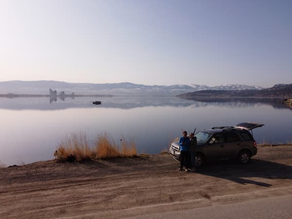 Claire & David at Okanagan Lake in Canada - @carnet_declaireurs 06/2024 David and Claire from @carnet_declaireurs standing beside their SUV with the trunk open, overlooking the serene Okanagan Lake in Canada. The calm lake reflects the distant mountains and clear sky, capturing the peaceful and scenic essence of their vanlife adventure. The image showcases the beauty of Okanagan Lake and the couple's love for travel and exploration.