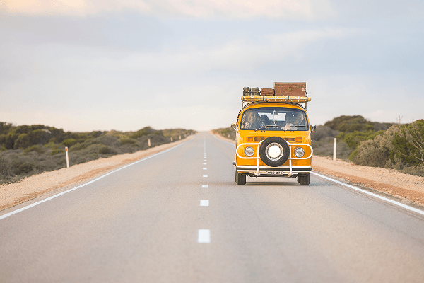 It is love of freedom and the soothing hum of the road - @summerofseventyfive 12/2022 A bright yellow 1975 Volkswagen Kombi camper van drives along a long, empty outback highway in Australia under soft evening light, with luggage and camping gear secured on the roof rack. The road stretches to the horizon, surrounded by low scrubland and open skies, symbolizing the freedom and adventure of long distance vanlife travel with family across the Australian landscape.