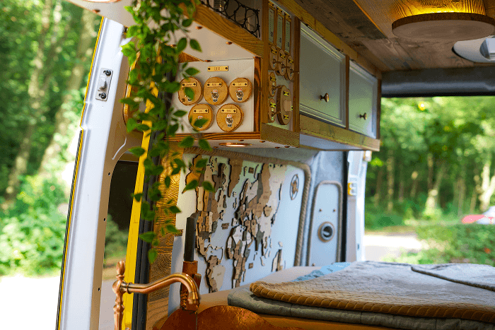 Interior view of our cozy custom van - @gary_and_sheila 06/2023 Interior view of a self converted Fiat Ducato camper van showing a cozy custom van build with wooden cabinets, a copper sink and faucet, hanging plants, and a world map wall panel above the bed. The image highlights DIY van conversion design, compact living, and full time vanlife details from the long term journey of @gary_and_sheila.
